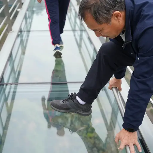 他怯生生地踏上了玻璃桥，手指紧扣栏杆发白。